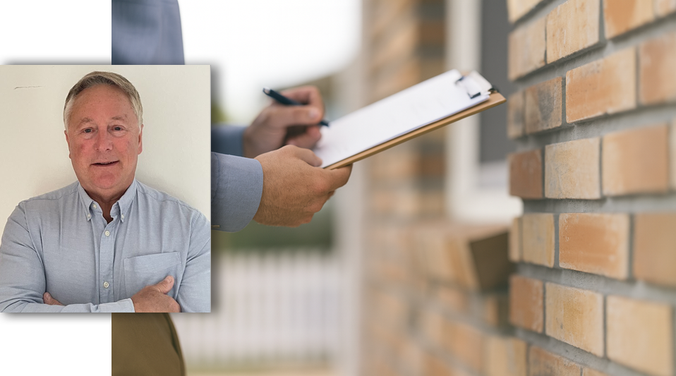 A surveyor with a clipboard making notes while standing next to a brick wall.