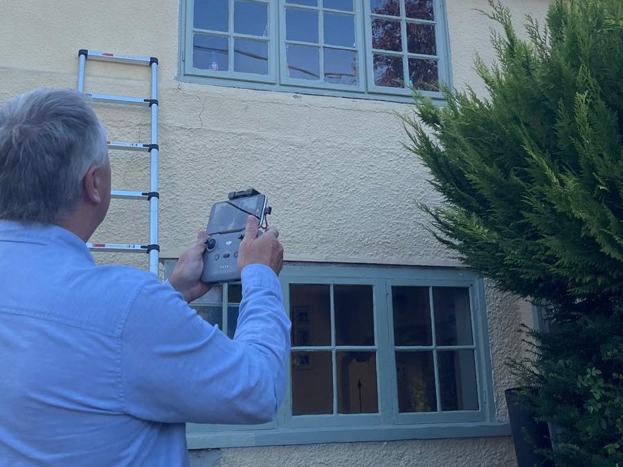 Surveyor operating a drone controller while inspecting a roof and upper elevation