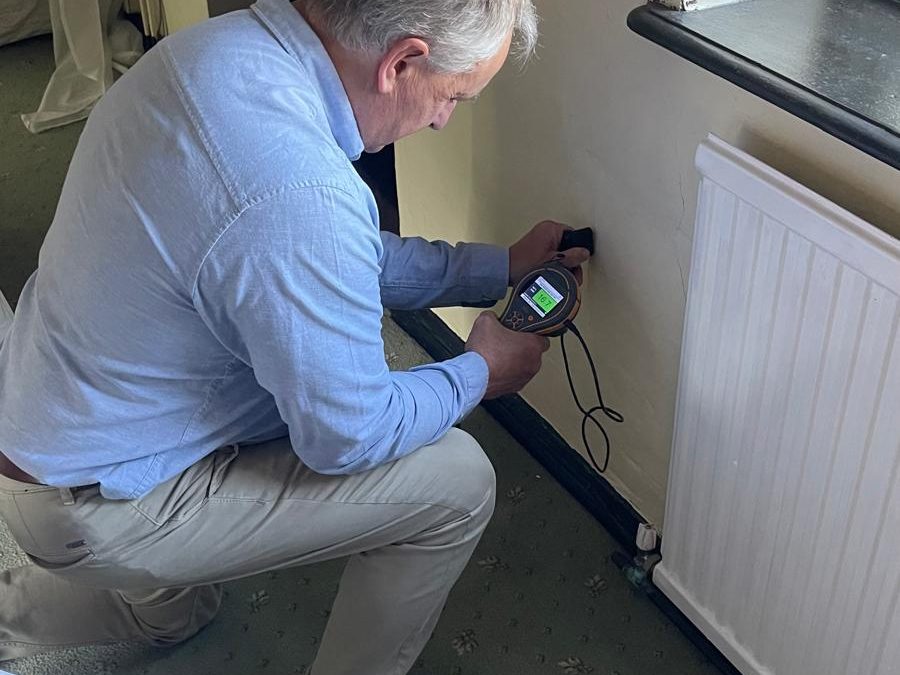 Surveyor taking a non-intrusive moisture reading beside a radiator