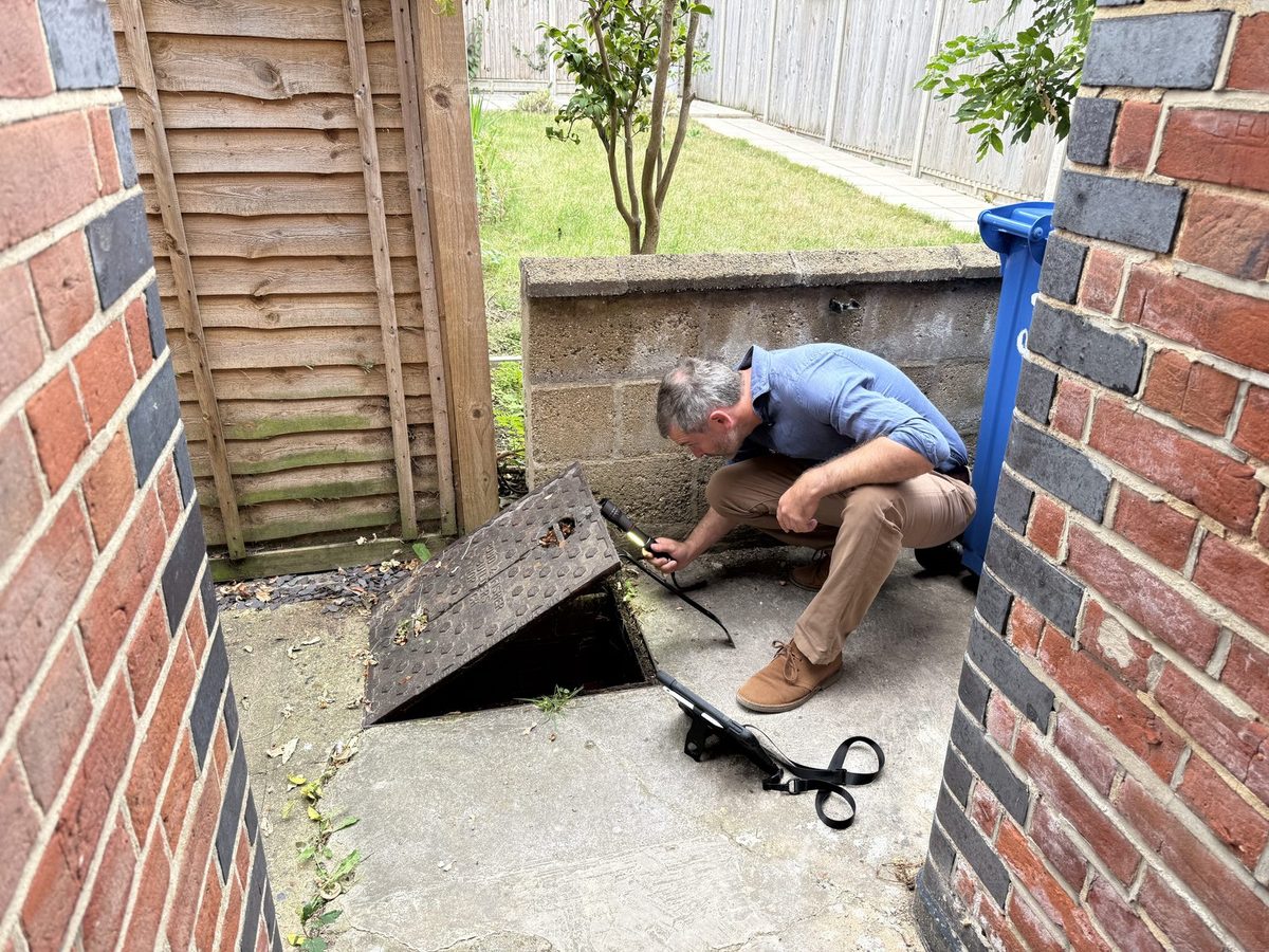 Surveyor inspecting drainage at a lifted inspection cover to the rear of a property