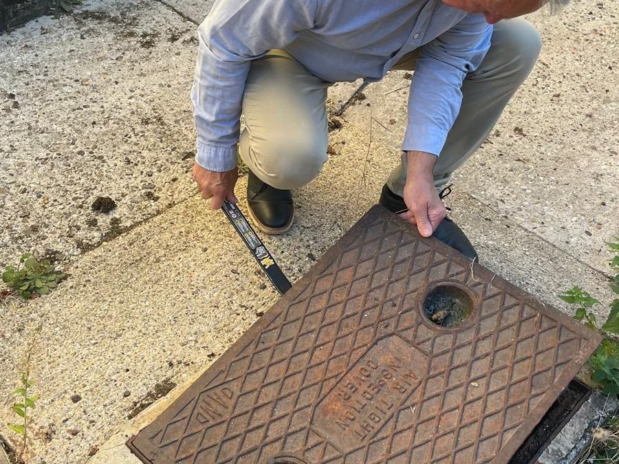 Surveyor lifting a cast iron inspection cover to record its condition